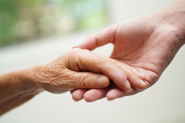 Giovane ragazzo asiatico che tiene la mano della donna anziana della nonna insieme con amore e cura