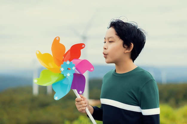 Giovane ragazzo asiatico progressista che gioca con il giocattolo della girandola del vento all'azienda agricola della turbina eolica