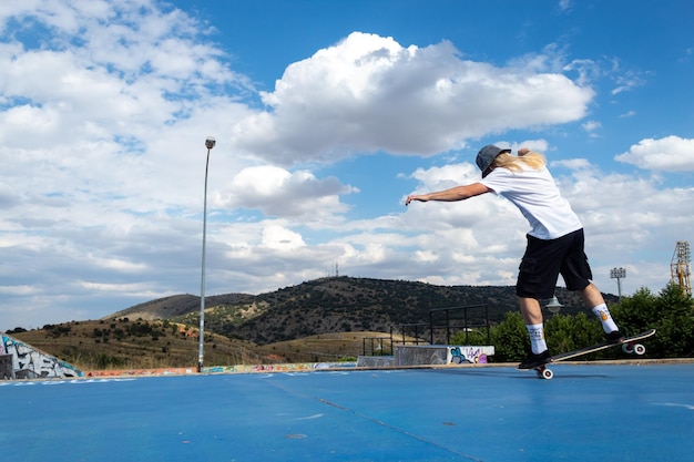 Giovane ragazzo biondo dai capelli lunghi che esegue acrobazie sullo skateboard nello skatepark