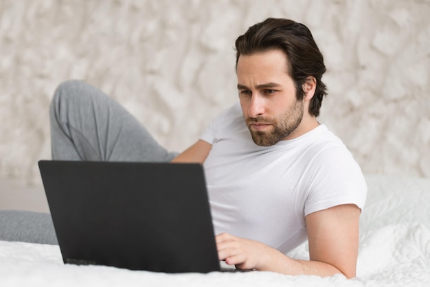 Giovane ragazzo caucasico concentrato serio sdraiato sul letto a guardare video sul computer che invia messaggi di testo online in camera da letto