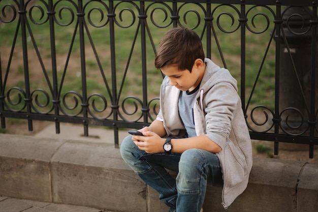 Giovane ragazzo che gioca con smaptphone Scolaro utilizzando il telefono cellulare sulla strada