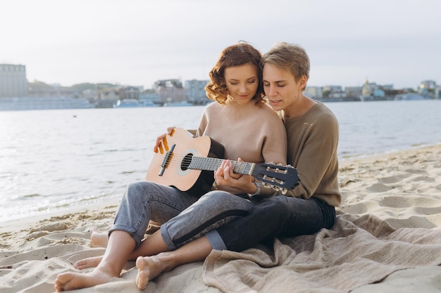 Giovane ragazzo che insegna alla sua ragazza a suonare la chitarra autodidatta Coppia innamorata che si diverte sulla spiaggia