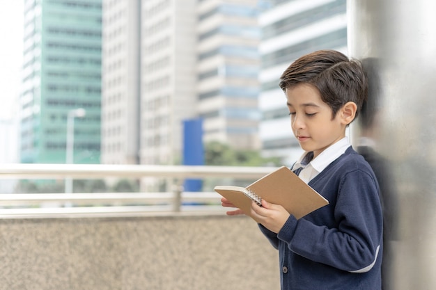 Giovane ragazzo che legge un libro sul distretto aziendale urbano, concetto di istruzione