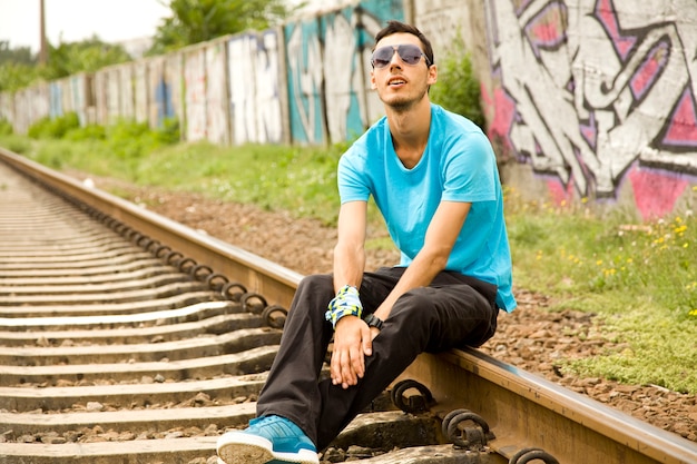 Giovane ragazzo con gli occhiali seduto alla ferrovia.