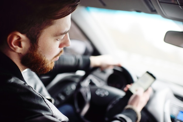 Giovane ragazzo con la barba compone un messaggio sullo smartphone in macchina