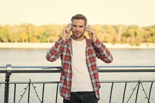 Giovane ragazzo con la barba lunga ascolta musica in cuffie modello di moda maschile all'aperto