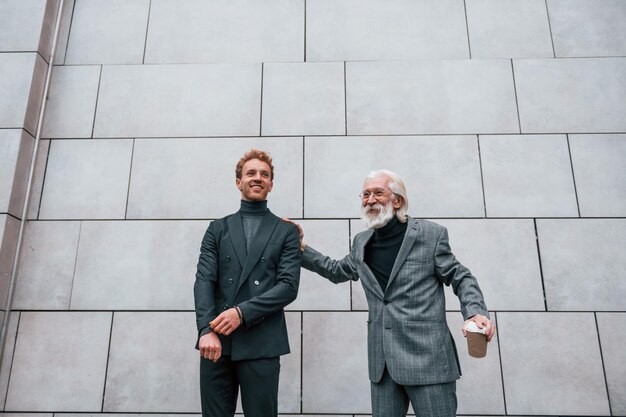 Giovane ragazzo con uomo anziano in abiti eleganti è insieme all'aperto Concezione del business