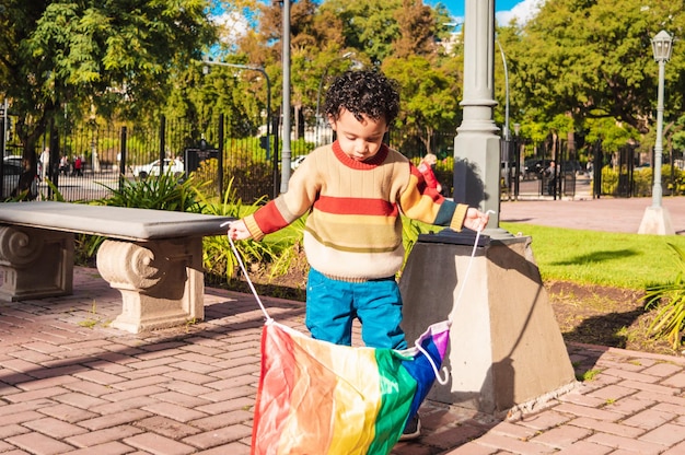 Giovane ragazzo dalla pelle marrone in una piazza urbana con una bandiera gay nelle sue due mani concetto lgbt