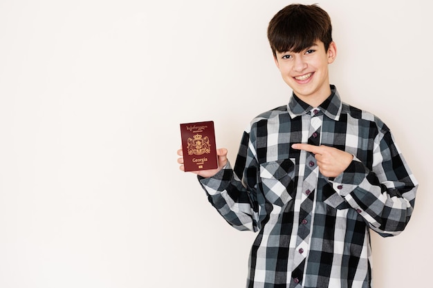 Giovane ragazzo dell'adolescente che tiene il passaporto della Georgia che sembra positivo e felice in piedi e sorridente con un sorriso fiducioso su sfondo bianco