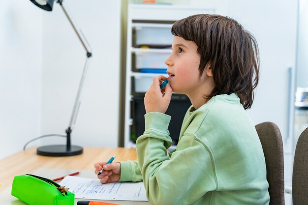 Giovane ragazzo della scuola che fa il suo lavoro seduto al tavolo a casa. bambino concentrato che pensa a un compito con piacere. Istruzione homeschooliong.