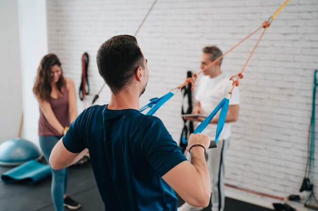 Giovane ragazzo e ragazza latino che fanno esercizi per le braccia con l'aiuto di un personal trainer