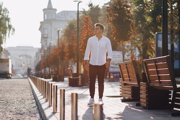 Giovane ragazzo elegante in una camicia che cammina per una strada europea in una giornata di sole