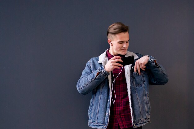 Giovane ragazzo elegante in una giacca di jeans e camicia ascoltando musica