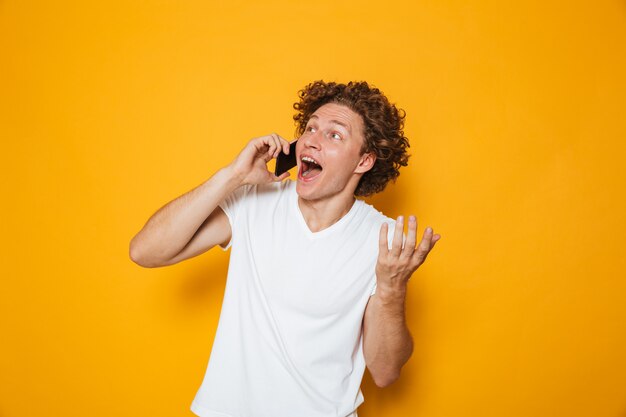 Giovane ragazzo felice con capelli ricci che grida e che parla sullo smartphone