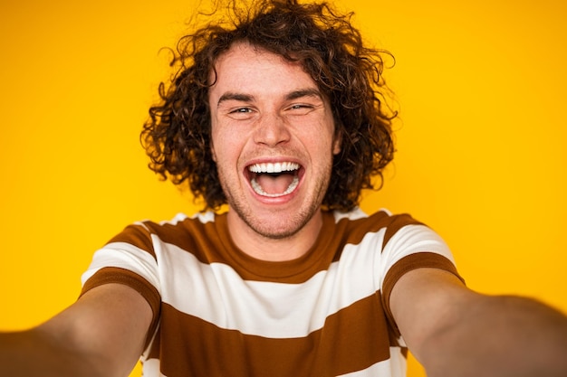 Giovane ragazzo gioioso che prende selfie e guarda l'obbiettivo in studio