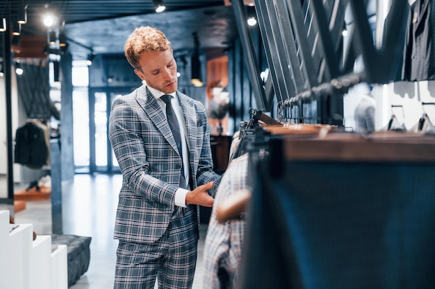 Giovane ragazzo in un negozio moderno con vestiti nuovi Abbigliamento elegante e costoso per gli uomini