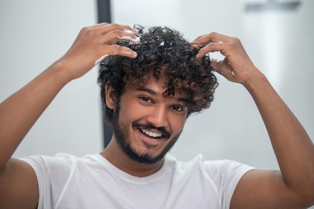 Giovane ragazzo indiano bello dai capelli ricci che si fa i capelli