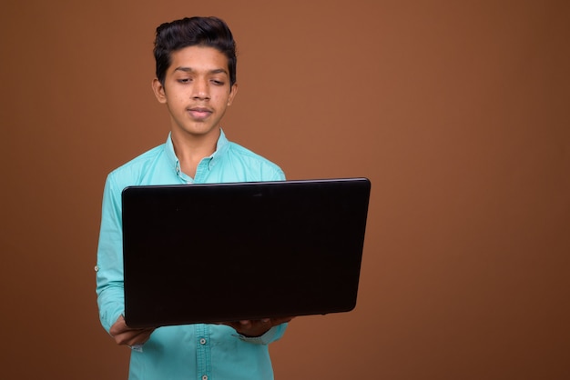 Giovane ragazzo indiano che indossa maglietta blu cercando smart contro sfondo marrone