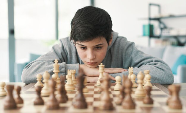 Giovane ragazzo intelligente che gioca a scacchi a casa è concentrato e guarda la scacchiera