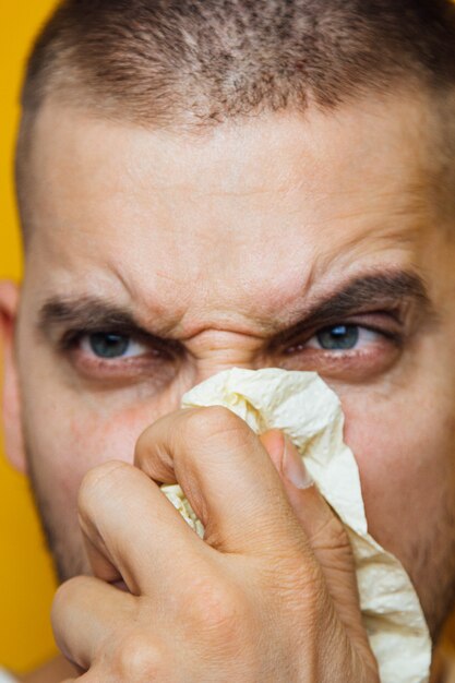 giovane ragazzo malato con un virus starnutisce nella carta igienica che tiene tra le mani. Stagione allergica, pandemia, raffreddori. Espressione facciale dispiaciuta.