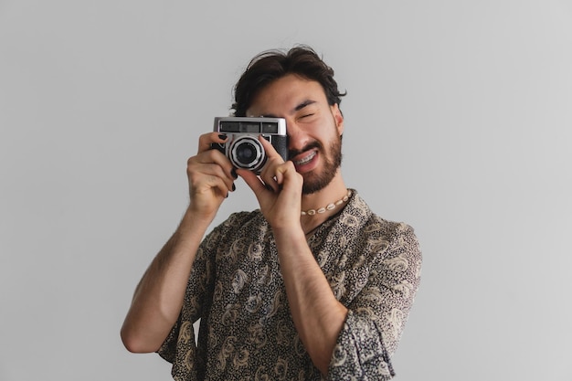 Giovane ragazzo queer latino gay che scatta foto con una vecchia macchina fotografica su sfondo bianco