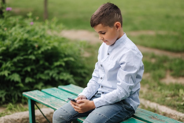 Giovane ragazzo seduto sulla panchina e giocare online durante le vacanze scolastiche