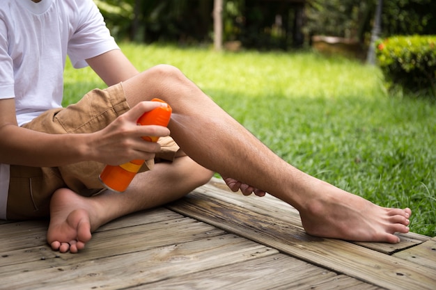 Giovane ragazzo spruzzare repellenti per insetti sulla sua gamba con flacone spray