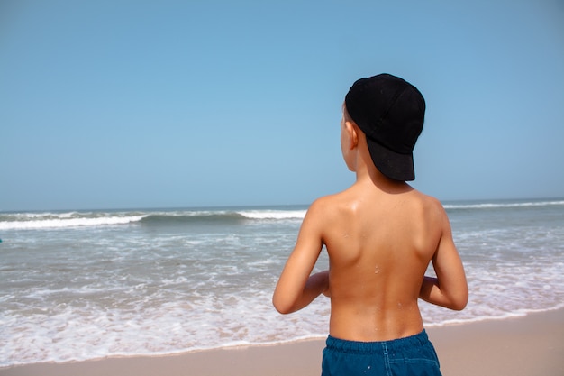 Giovane ragazzo sulla spiaggia a fissare l'acqua