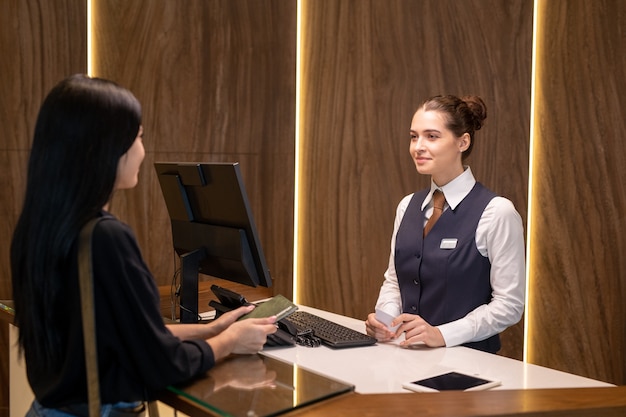 Giovane receptionist femminile che serve uno dei clienti al bancone