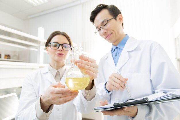 Giovane ricercatore femminile che tiene il becco con liquido giallo mentre lo mostra al collega durante l'esperimento scientifico in laboratorio