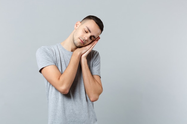 Giovane rilassato in abiti casual che riposa, dorme con le mani vicino al viso, tenendo gli occhi chiusi