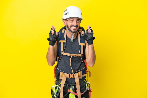 Giovane rocciatore caucasico uomo isolato su sfondo giallo con le dita incrociate