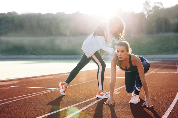 Giovane runner femminile con personal trainer che si prepara per il lancio nella nebbia sulla pista sportiva