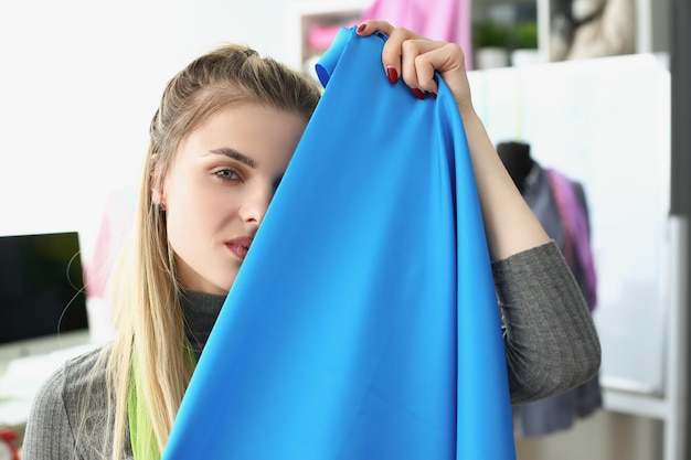 Giovane sarta donna che si nasconde dietro un tessuto blu di alta qualità