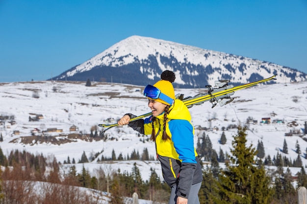 Giovane sci grazioso sorridente della tenuta della donna. montagne sullo sfondo. viaggio invernale