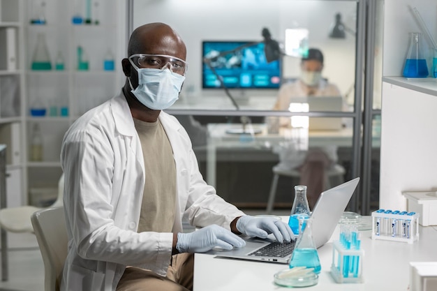 Giovane scienziato maschio afroamericano che digita durante il lavoro in laboratorio