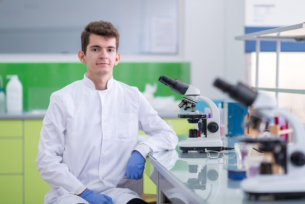 Giovane scienziato studente che guarda attraverso un microscopio mentre fa alcune ricerche in laboratorio