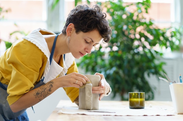 Giovane scultrice crea stoviglie in ceramica in studio donna artista della ceramica lavora con argilla bagnata