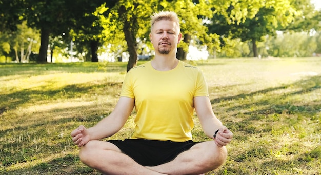 Giovane seduto su un tappetino da yoga in posizione di loto con gli occhi chiusi che si prepara a praticare lo yoga