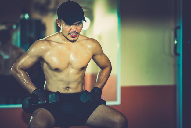 Giovane senza camicia che solleva manubri in palestra