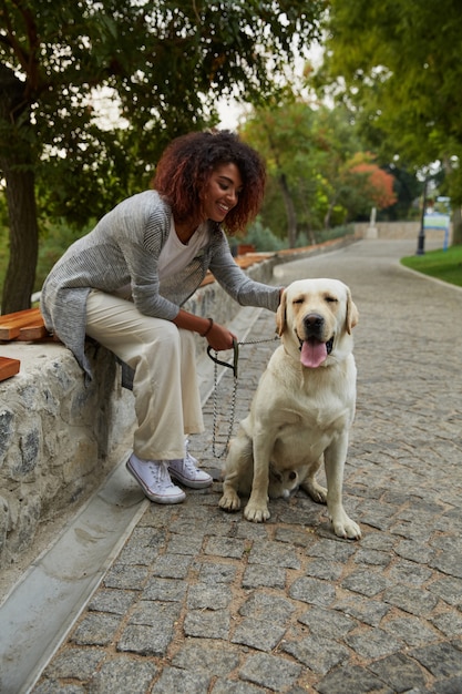 Giovane signora graziosa che si siede con il cane amichevole in parco
