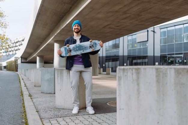 Giovane skater sorridente che tiene longboard Felice uomo caucasico che indossa abiti casual Foto di alta qualità