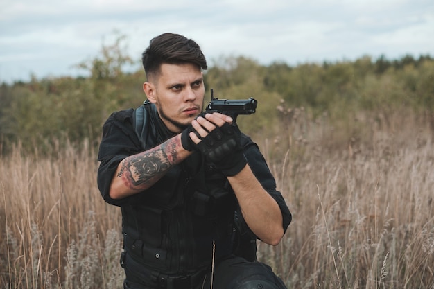 Giovane soldato in uniforme nera che si siede e che mira una pistola