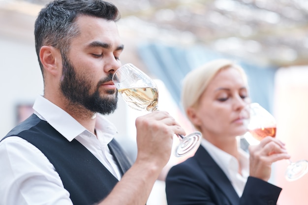 Giovane sommelier maschio barbuto e la sua collega annusando nuovi tipi di vino in bicchieri da vino prima di assaggiarlo