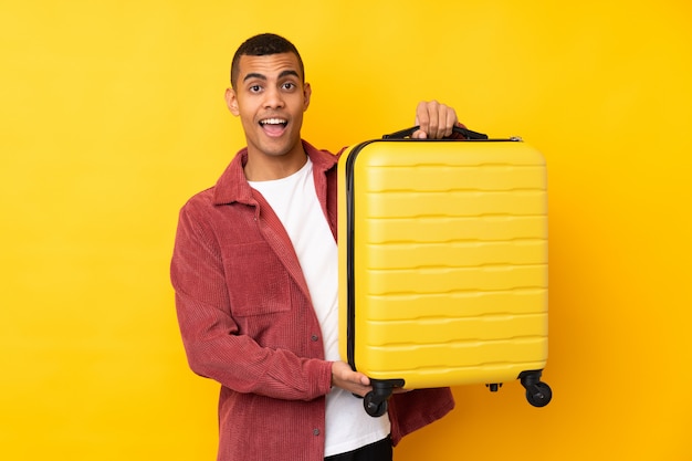 Giovane sopra la parete gialla isolata in vacanza con la valigia di viaggio