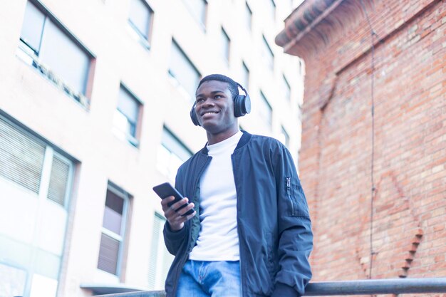 Giovane sorridente che ascolta musica mentre usa il telefono fuori dall'edificio