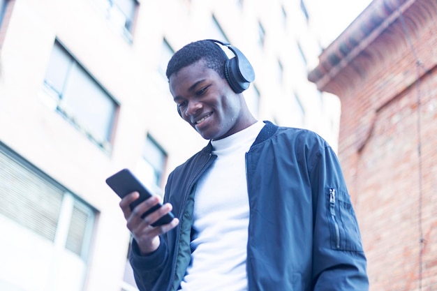 Giovane sorridente che ascolta musica mentre usa il telefono fuori dall'edificio