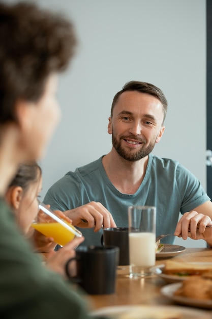 Giovane sorridente che fa colazione servendo il tavolo da pranzo e guarda sua moglie mentre la ascolta durante la discussione sui piani per la giornata