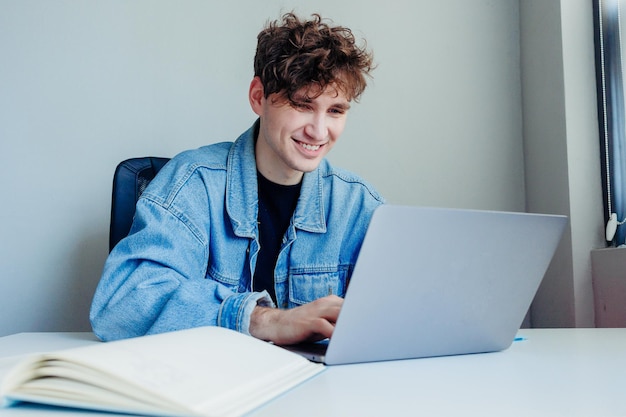 Giovane sorridente che lavora sul suo computer portatile Libero professionista in ufficio oa casa che lavora