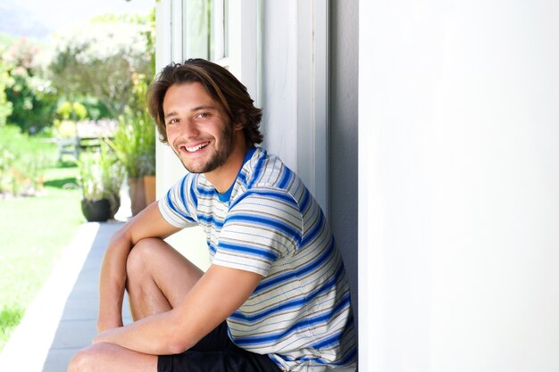 Giovane sorridente che si siede sul patio fuori